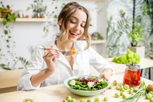 Femeie zâmbitoare care mănâncă o salată proaspătă de legume